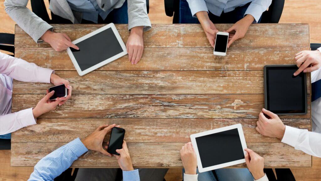 Personnes tenant leur portable ou tablette au dessus d'une table
